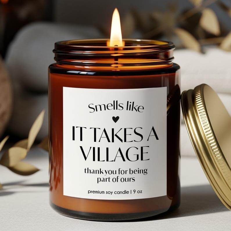 Thank you gift candle with a warm glow, labeled 'Smells like IT TAKES A VILLAGE, thank you for being part of ours'. 9 oz premium soy candle.